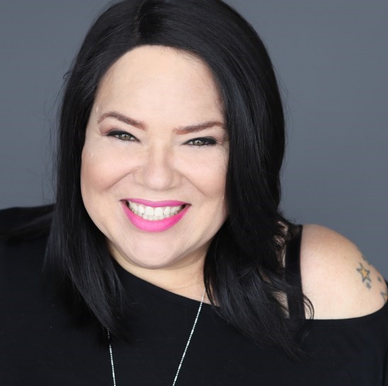A person with dark hair and a black shirt smiles at the camera.
