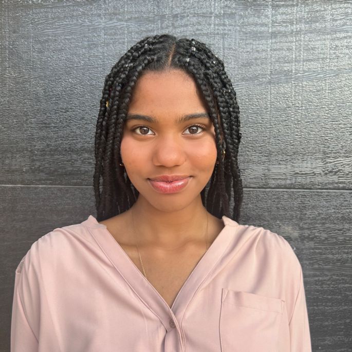 202 Madison Poet Laureate Maliha Nu'Man in a print long sleeve button up shirt against aa grey backdrop.