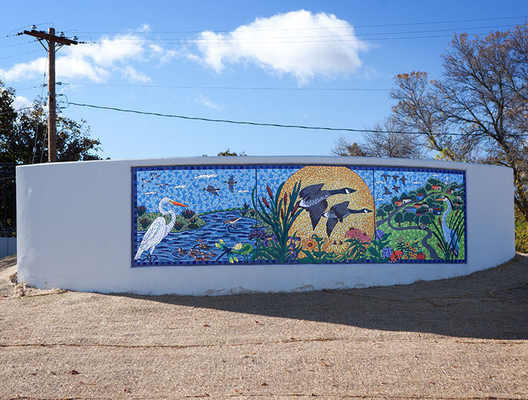 A mural showing a scene with water, a large sun and a neighborhood with abundant birds.
