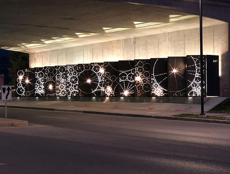 A series of illuminated panels with circles positioned under an overpass at night.