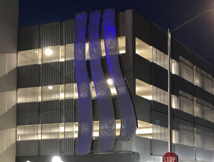 Three virtical blue waves on the side of a parking garage.