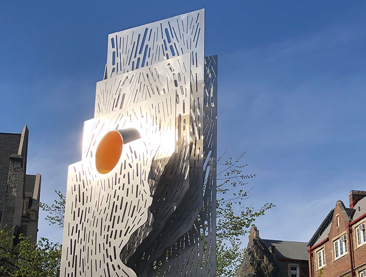 Vertical structure with 5 layers of silver metal of varying sizes with an orange circle at the top of the front panel.