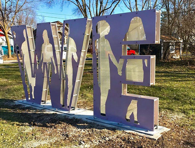 Scupture that spells WE with silhouettes of people holding hands inside the letters.