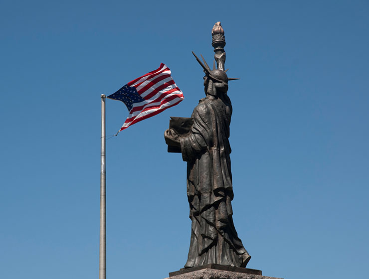 Statue of Liberty set against a blue sky and an American flag.