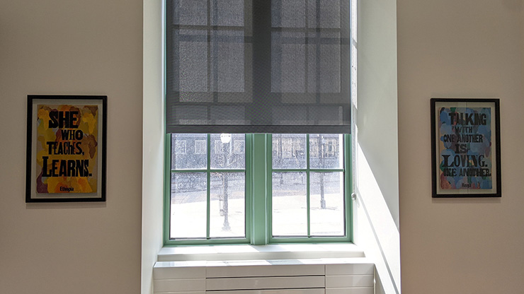 Two prints on either side of a green-framed window. The print on the left reads 'She who teaches learns' and the print on the right reads 'Talking with on another is loving one another.'