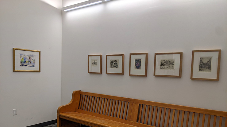Six framed art peices in a corner above a wooden bench.