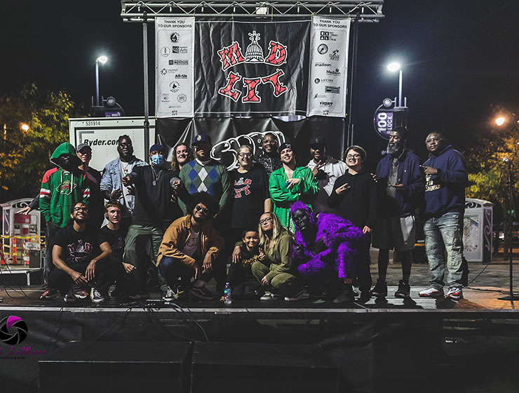 A group of people posing on a stage in front of a Mad Lit banner at night.