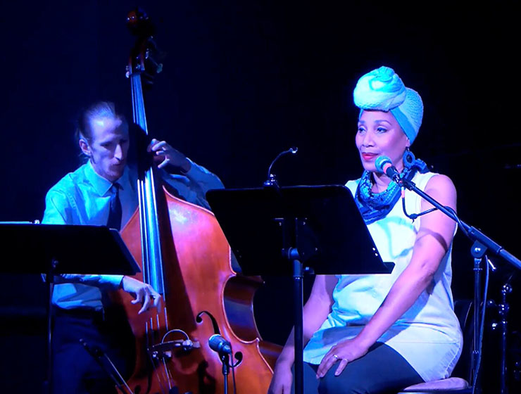 Two performers on a stage, Sam Olson playing an upright bass and Quanda Johnson with a microphone.