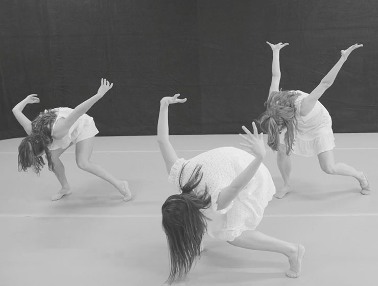 Three unidentified ballet performers posing with their heads towards the white floor and arms up in the air.