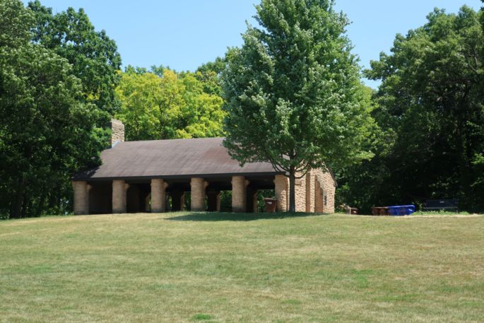 Park shelter up grassy hill with trees. 