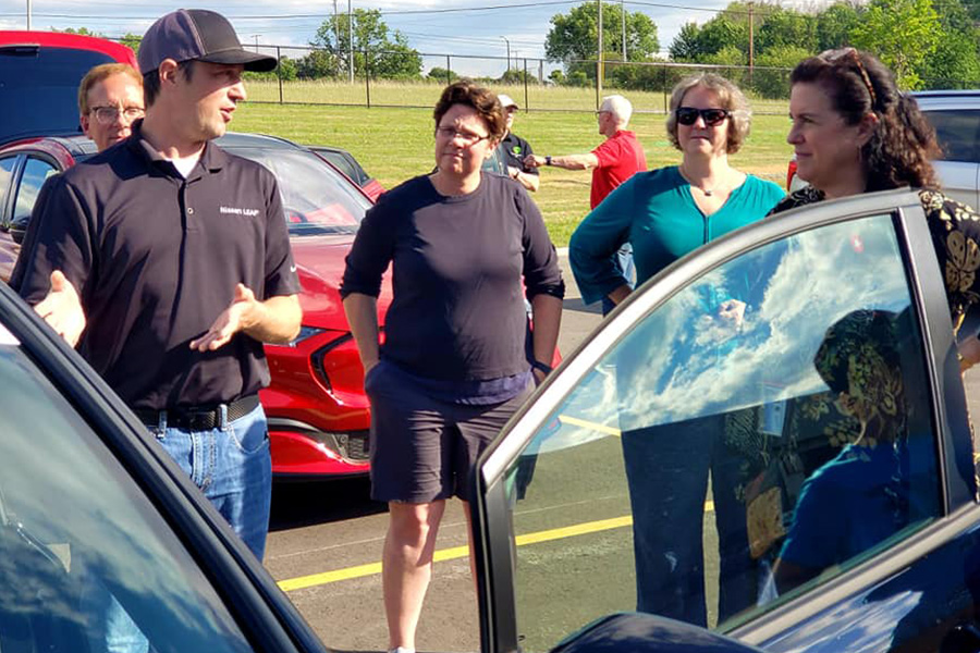 A group discusses electric vehicles on display with Mayor Satya