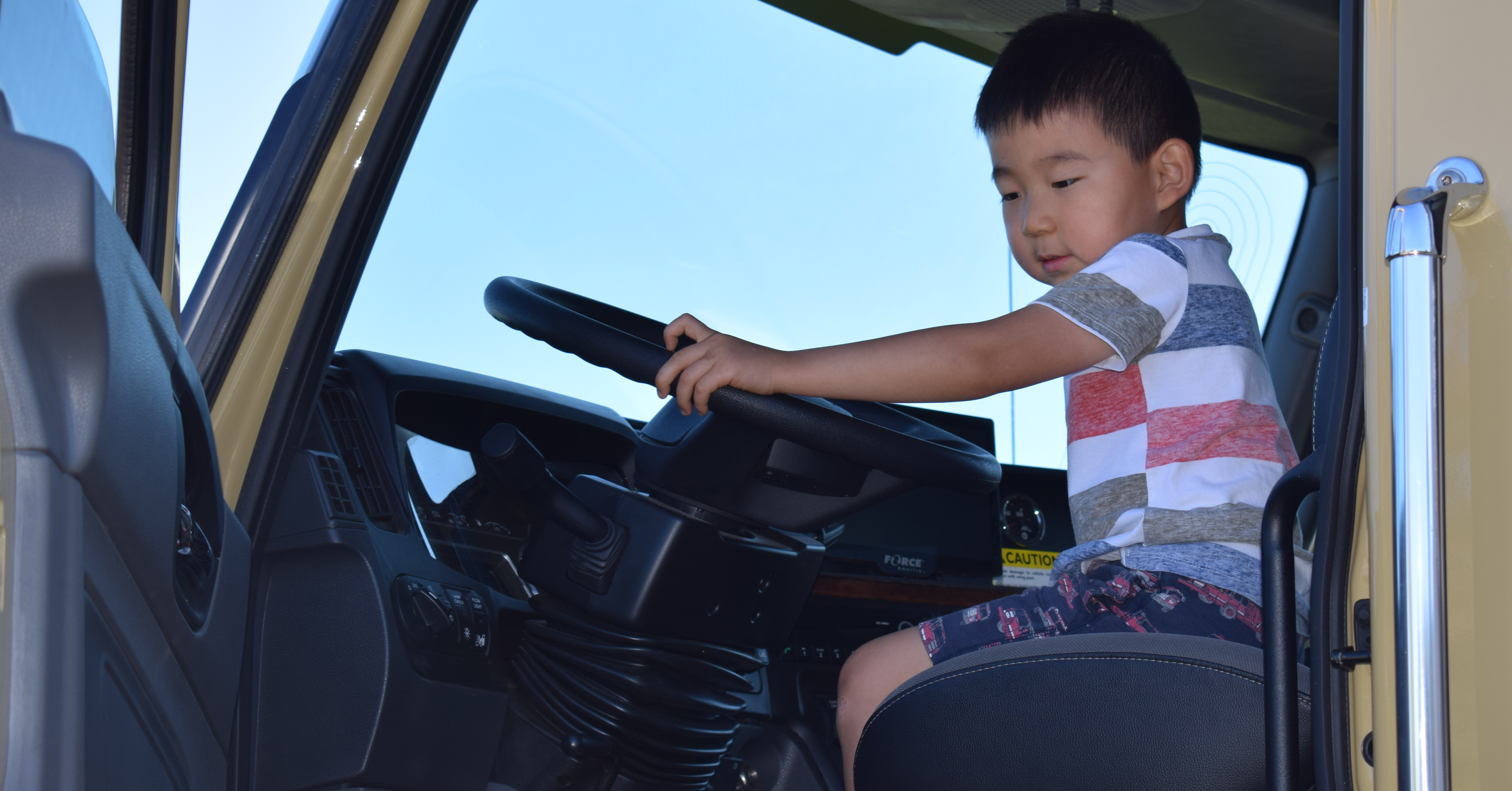 child sitting in big truck with hands on steering wheel