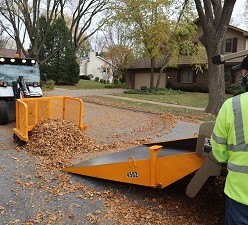 A toolcat is pushing fall leaves onto a pan truck.