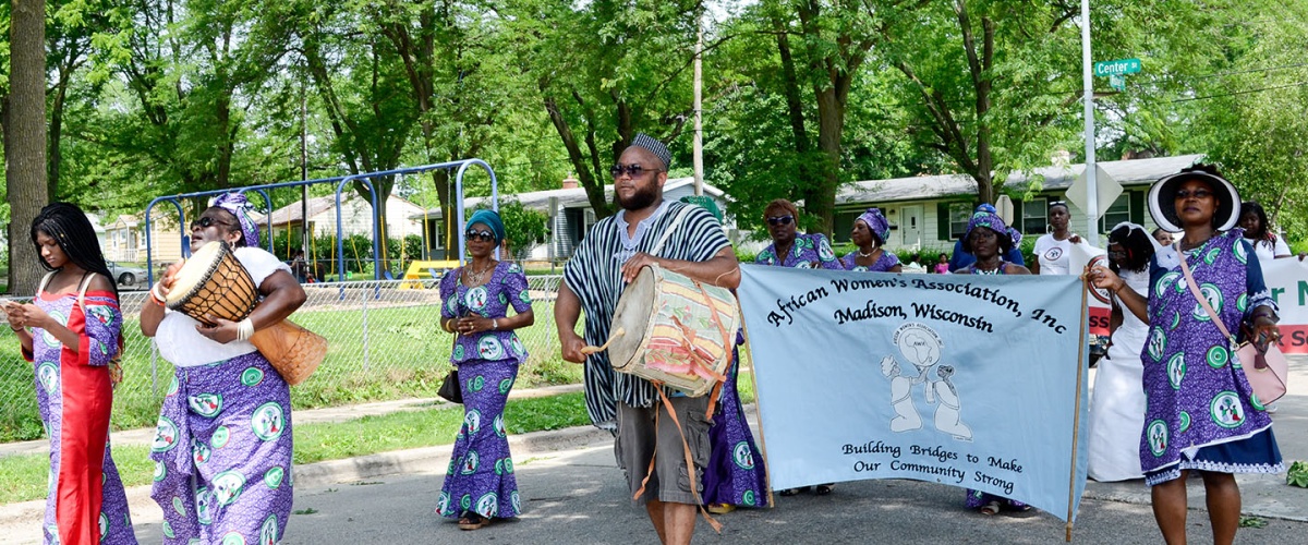Group of Black people walking in a parade. Two people are holding a banner for the Madison, Wisconsin African Women's Association.