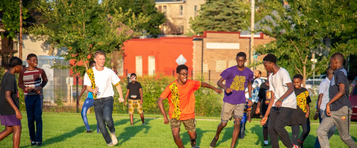 Group of children and teenagers, mostly Black, play soccer at Africa Fest. Their faces are excited, focused, and smiling.