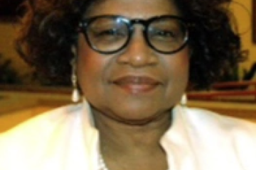 Alder Barbara Harrington-McKinney, of African American descent, is wearing a white blazer, black shirt, white pearls and black rimmed glasses.