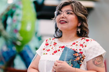 Author, business owner, and poet Araceli Esparza stands holding her book.