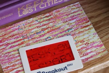 A book, colorful sheet of paper and decoder with red transparency and the word "breakout" on it lie on a table. 