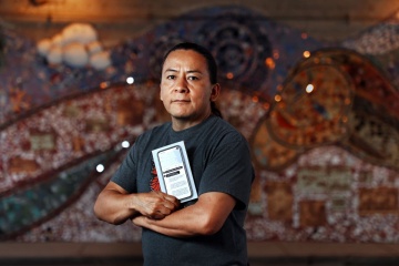 Storyteller and author Nestor Gomez stands with crossed arms, holding his book.