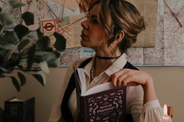 A woman sits holding an Agatha Christie book and looking off into the distance. 