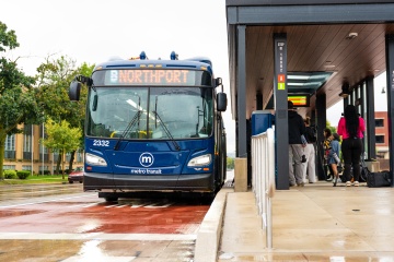 Metro electric bus docked at a BRT station on a rainy day.