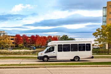 White paratransit vehicle driving down a road in autumn.