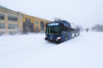 A metro bus travels along a snow-covered road during a snowstorm.