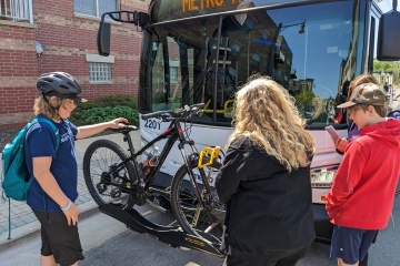 Students loading bicycle onto a Metro Transit bus bike rack.