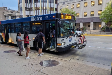 Students boarding Metro bus with a bicycle, with “R1 Junction” displayed on the marquee. 