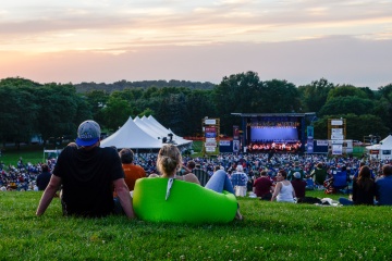 people sitting in a park watching a large stage with tents around it