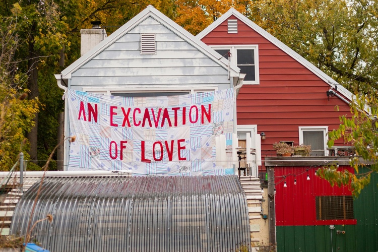 A large quilt hanging on a building that reads, "An Excavation of Love"