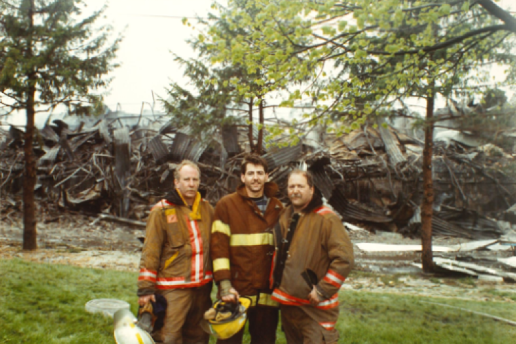 Three firefighters stand in front of the fire-damaged Central Storage property