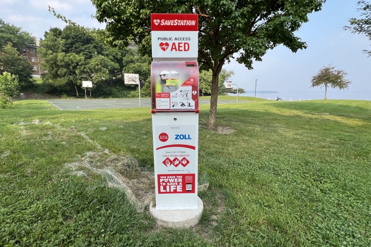 AED SaveStation situated in the grass with a basketball court behind it