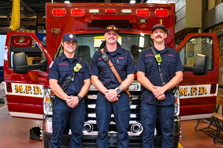 Three paramedics stand in front of the ambulance