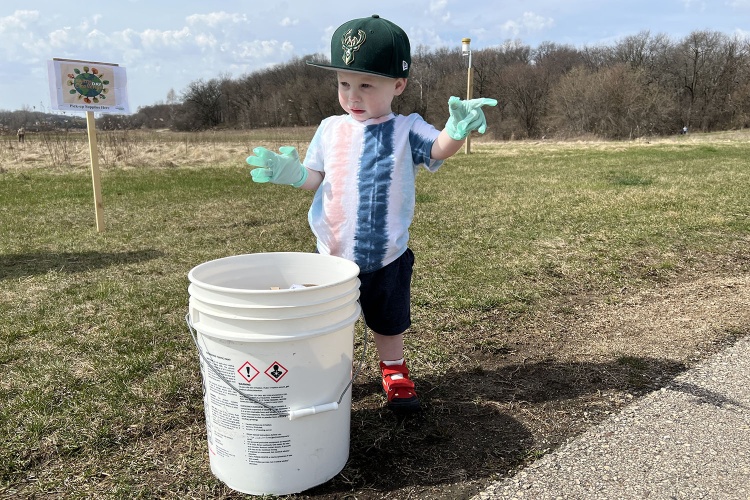toddler standing near bucket pointing with gloves on