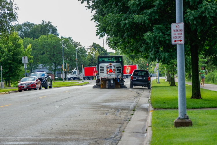 A street sweeper goes around a car parked in a spot where the car should not be parked. 