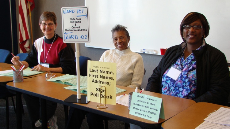 Three smiling election officials at a polling place.