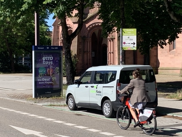 A bicicylist riding past a car that is part of a carshare