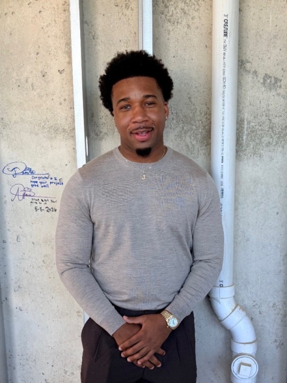 Julian Walters is wearing a gray shirt with a cement wall behind him.