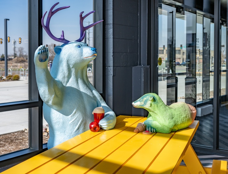 Sculpture of a bear with antlers and a raccoon sitting on a picnic table