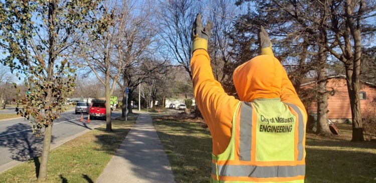 City employee in bright yellow vest with hands above head motioning distance while performing preventative Maintenace process of cleaning sewers