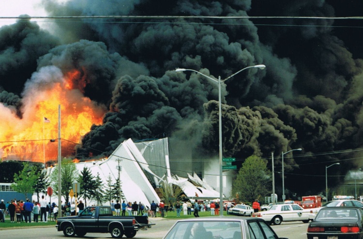 Crowds gather around the block with blaze of fire and large plumes of black smoke rising in the air