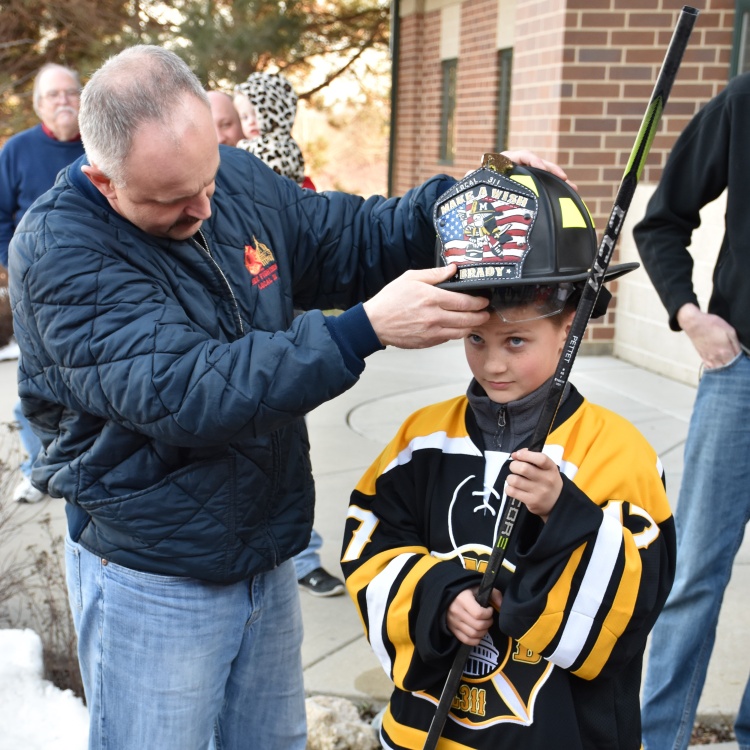 Lt. Thomas places a fire helmet on a Make-A-Wish child's head