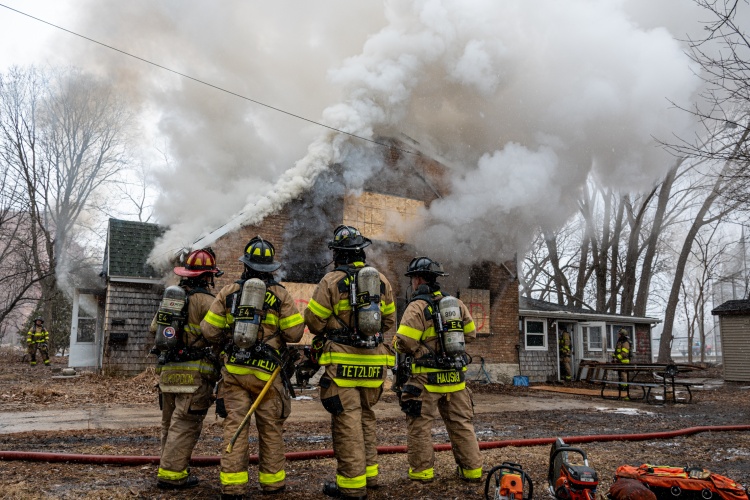 Firefighters look on as smoke billows from the house