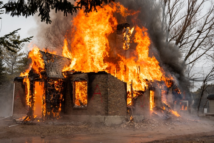 Flames engulf the house, with many structural components crumbled to the ground