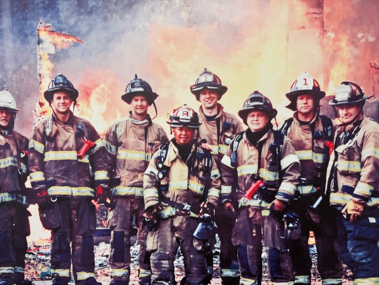 Bavery and others stand in front of a training house burn