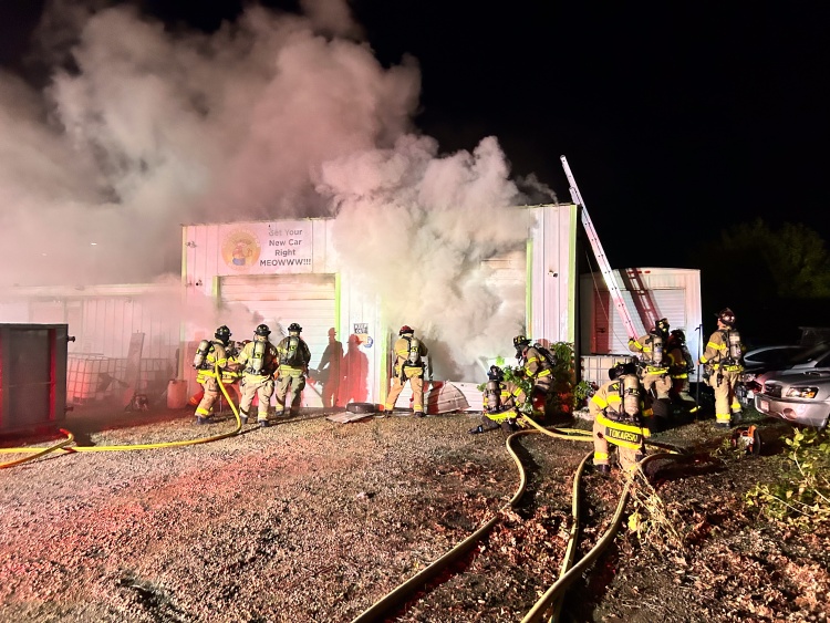 Firefighters advance hoses as smoke billows from auto repair shop