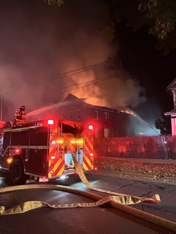 Fire truck in the street with firefighters flowing water onto house as smoke rises from roof