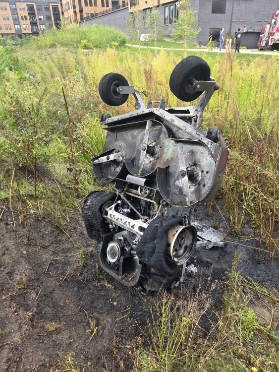 the remains of a riding lawnmower standing vertically in a ditch