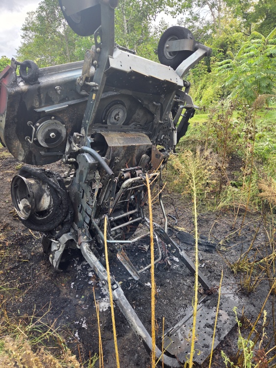 the remains of a riding lawnmower standing vertically in a ditch